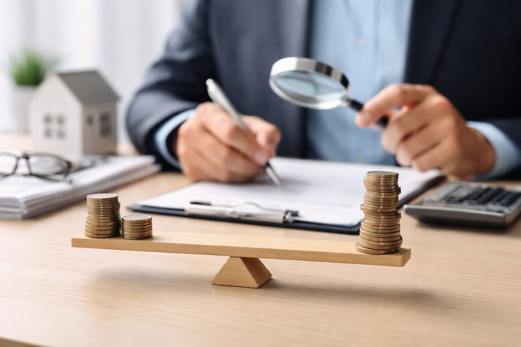 Foto de profissional analisando documentos financeiros com lupa enquanto compara pilhas de moedas em uma balança, representando análise de custos, equilíbrio financeiro, juros e planejamento econômico.