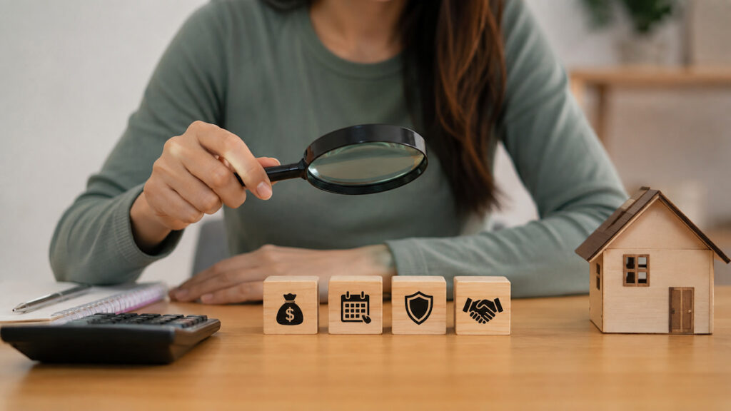 Mulher usa uma lupa para analisar símbolos de dinheiro, prazo, proteção e acordo, ao lado de uma casa em miniatura e uma calculadora, representando a comparação cuidadosa de ofertas de empréstimo.